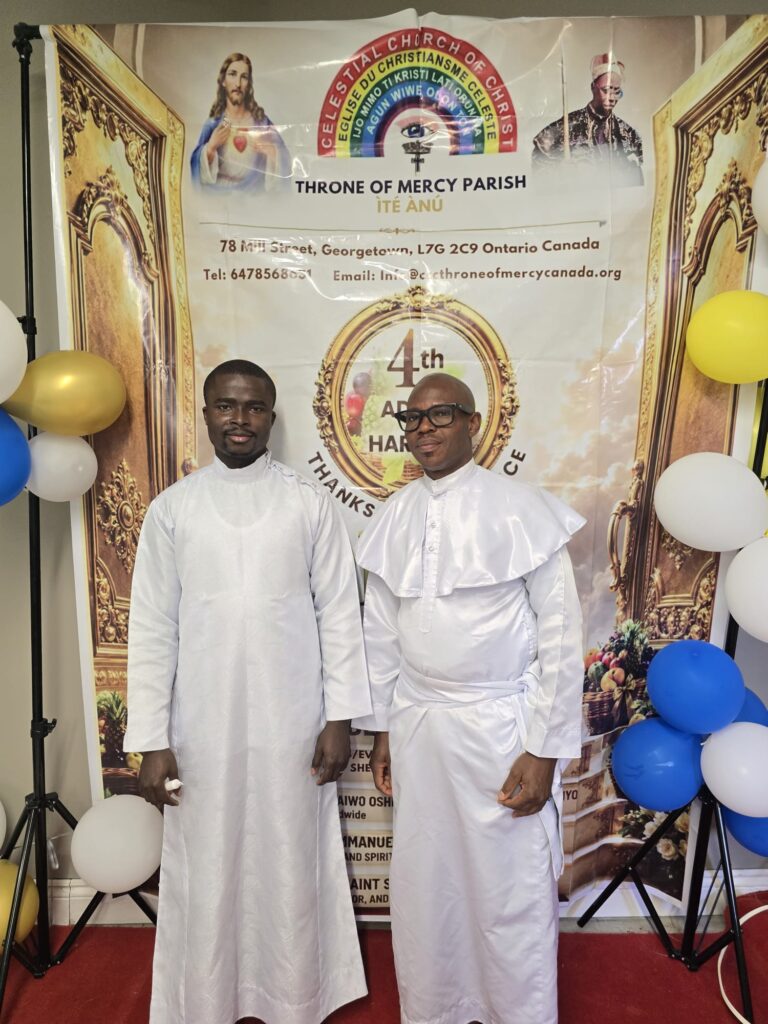 Two clergy members in white garments at the harvest thanksgiving banner