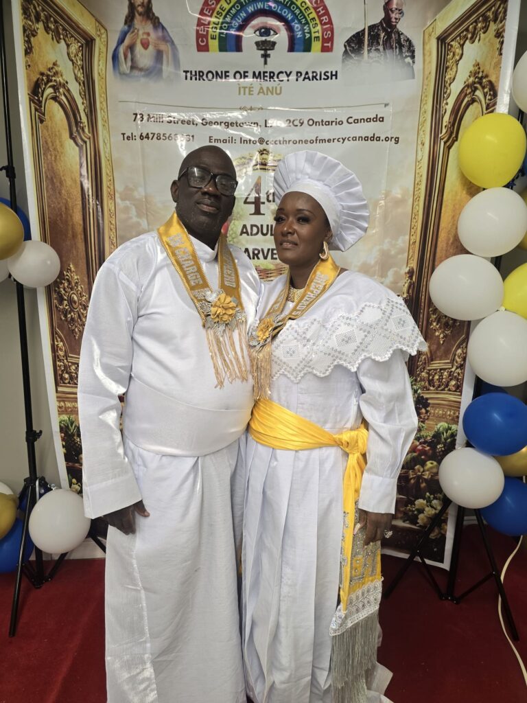 Two celebrants in white garments with gold harvest sashes at the harvest banner