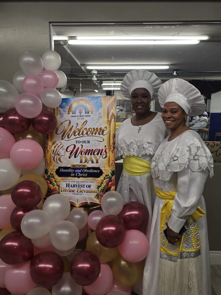 Two women in white garments and head coverings beside the Women's Day welcome sign