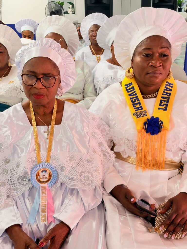 Two women in white, one wearing a Divine Elevation rosette and one a Harvest Adviser sash