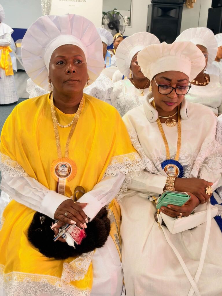 Two women in white head-ties wearing Divine Elevation rosettes